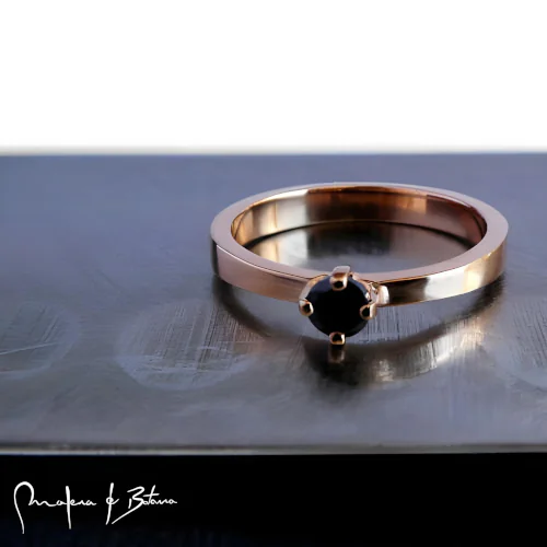 Anillo de compromiso con piedra central oscura en un aro de oro rosa.