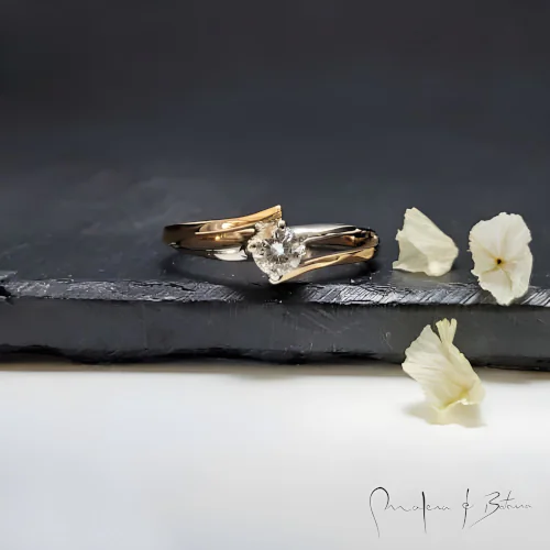 Anillo de compromiso en oro bicolor con diamante solitario y diseño de bandas entrelazadas