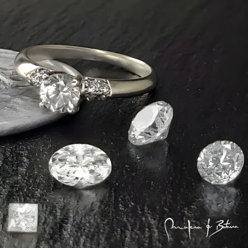 Imagen de un anillo de compromiso de diamantes con una piedra central en talla redonda y piedras laterales engastados en la banda. Se muestran diamantes sueltos en tallas redonda, oval y princesa para opciones de personalización.