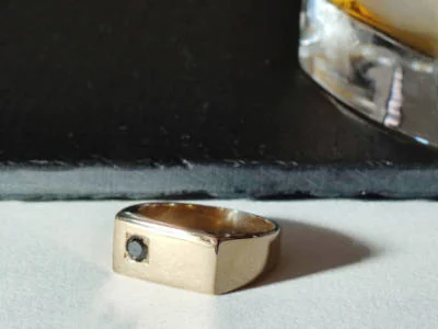 Imagen de un anillo de oro amarillo con un diamante negro engastado en una placa rectangular, modelo #2019 de Malena de Botana.