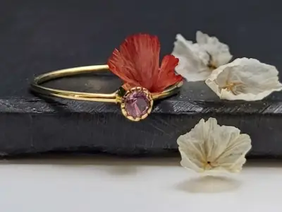 Anillo de oro con una pequeña piedra rosa y un adorno floral rojo. Número de artículo: #2201.