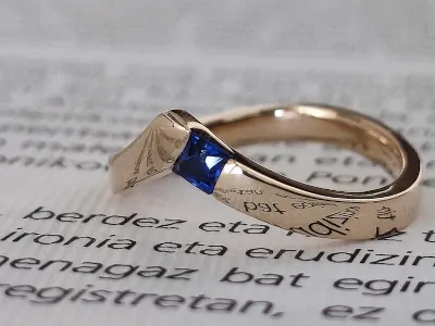 Anillo de oro amarillo con zafiro azul y una inscripción grabada en la banda, modelo #2223 de Malena de Botana.