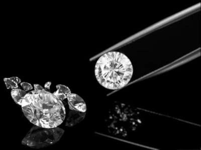  Imagen en blanco y negro que muestra varios diamantes brillantes, con un diamante redondo siendo sostenido por pinzas, sobre un fondo oscuro que resalta su claridad y brillo.