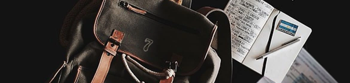  Imagen que muestra una mochila de cuero con detalles en cuero marrón, acompañada de una libreta, un bolígrafo, monedas y documentos de viaje, sobre un fondo oscuro, creando una atmósfera de aventura y exploración.