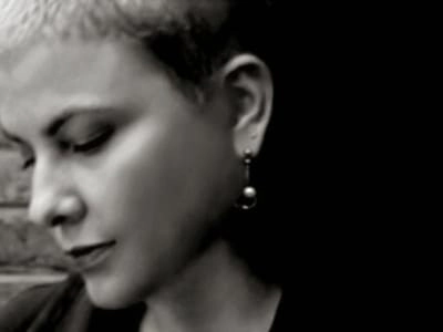 Imagen en blanco y negro de una mujer con cabello corto y aretes, mirando hacia abajo, destacando su expresión contemplativa.