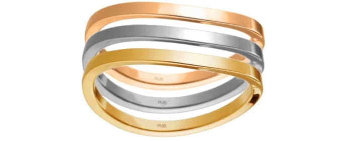 Conjunto de tres anillos de oro de diferentes colores: amarillo, blanco y rosa. Los anillos están entrelazados y tienen una forma ligeramente curvada.