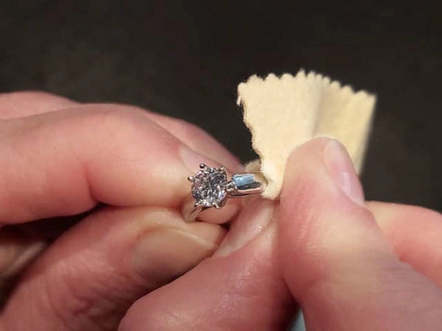 Primer plano de manos limpiando delicadamente un anillo de compromiso con diamante utilizando un paño suave, demostrando técnicas adecuadas de cuidado para joyería